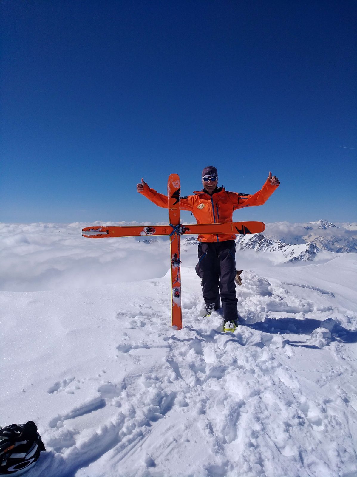 Harald Prey am Gipfelkreuz mit aufgestellten Freerideski ueber dem Wolkenmeer