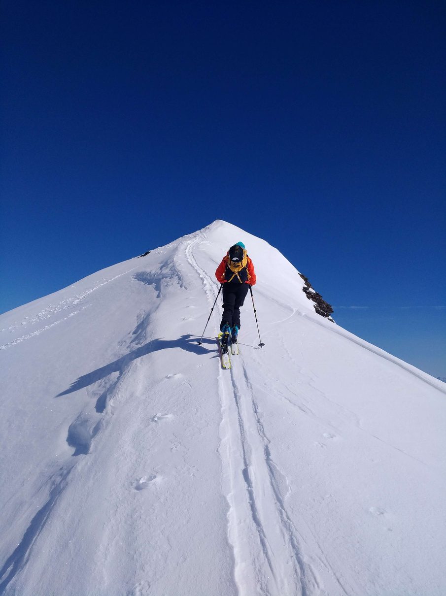 Skitourengeher steigt entlang eines schmalen Schneegrats zum Gipfel auf